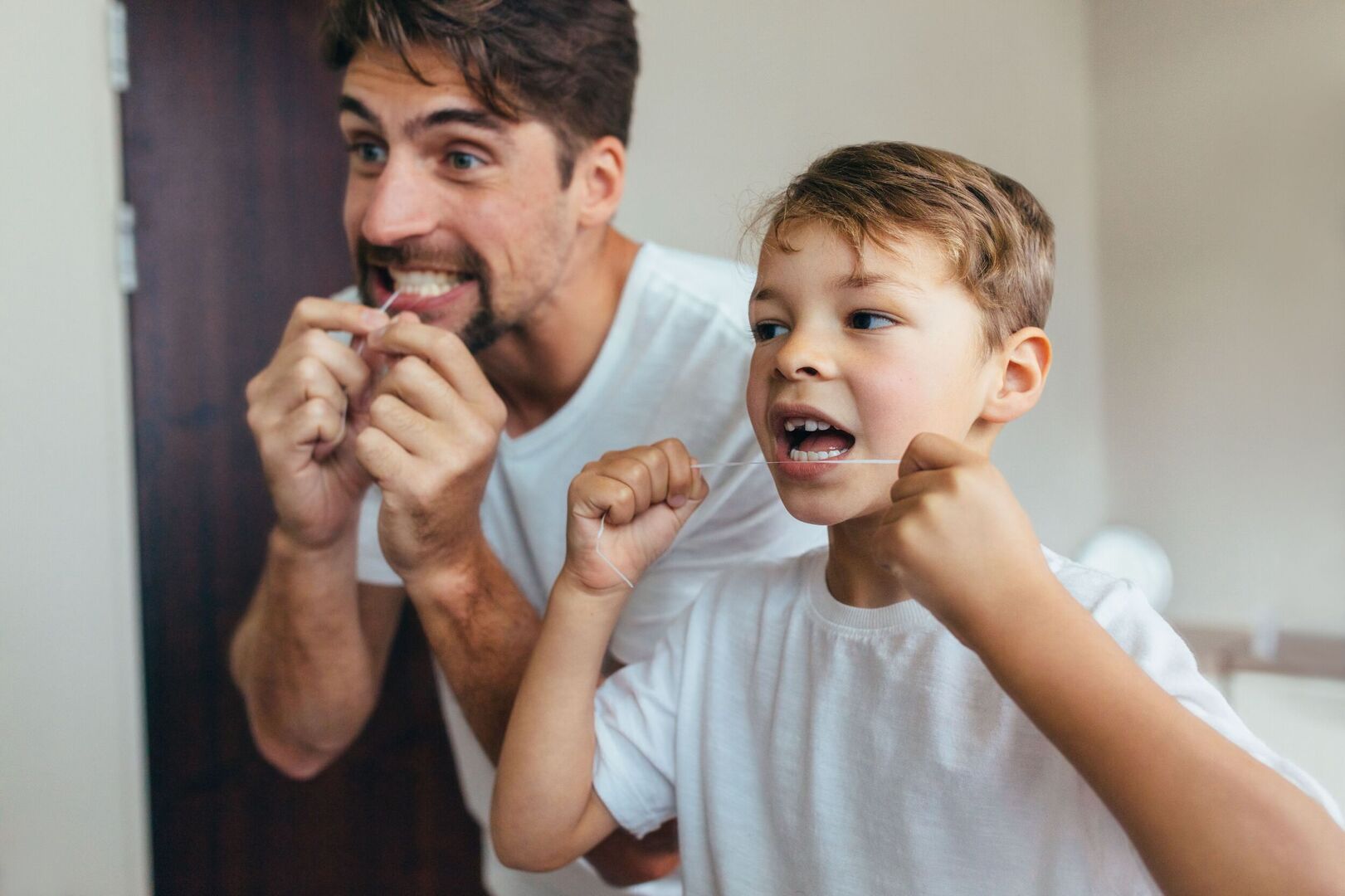 Vater und Kind reinigen gemeinsam ihre Zahnzwischenräume mit Zahnseide